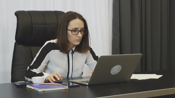 Woman works on laptop using computer mouse in modern office 