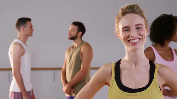 Beautiful woman smiling while her group talking in background in fitness studio