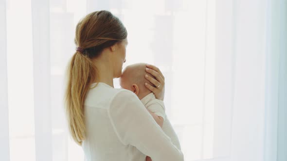 Back View of the Caucasian Mother Holding and Swings Her Newborn Baby Before Sleeping and Telling