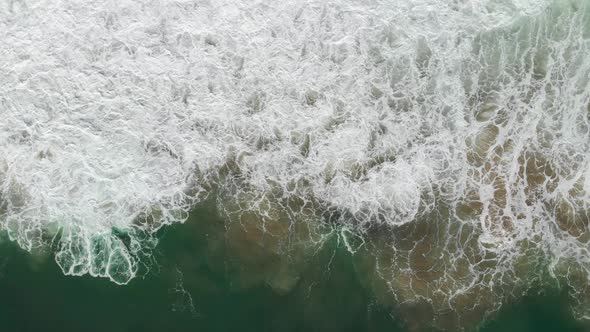 Top-down slow aerial shot following the ocean waves as they crash on the California shore near Monta