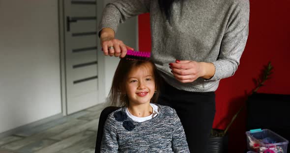 Mother combing, brushing her daughter's hair at home, woman and girl smiling, love, care