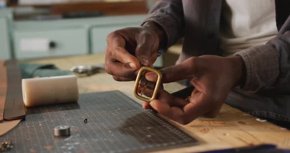 Hands of african american craftsman using tool to make a belt in leather workshop