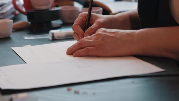 An Elderly Woman Designer Sketching on the Paper Using a Ruler