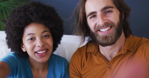 Portrait of mixed race couple blowing kisses on videocall while sitting on the couch at home