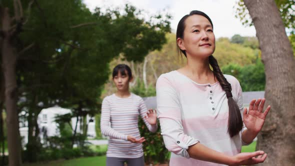 Happy asian mother exercising in garden with daughter, practicing tai chi together