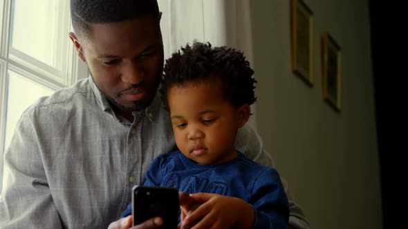 Front view of black father and son using smartphone in a comfortable home 4k