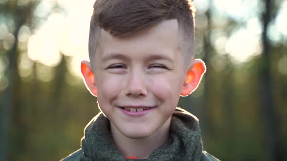 Cute Boy Looking at Camera While Standing on Blurred Background of Forest in Countryside