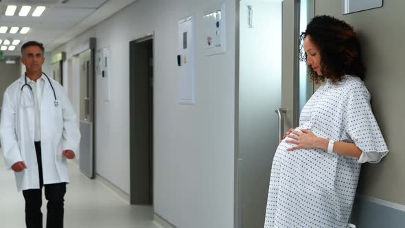 Pregnant woman touching her belly while doctor walking in corridor