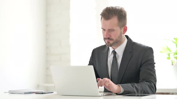 Young Businessman Showing Thumbs Up Sign While Using Laptop in Office