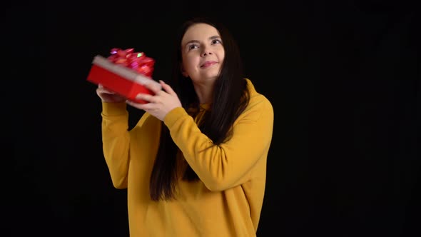 Young Woman with a Gift Box on Black Background. Gift Box with White Ribbon for Happy New Year