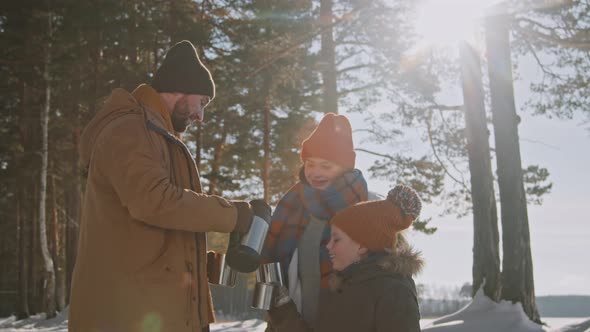 Family Warming Up with Hot Tea on Hike in Winter