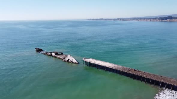 Concrete ship SS Palo Alto wreck near wooden pier, aerial rotate view. Sandy beach and endless ocean