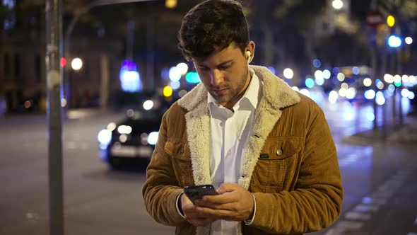 Man with Earphones Using Cellphone Near Road