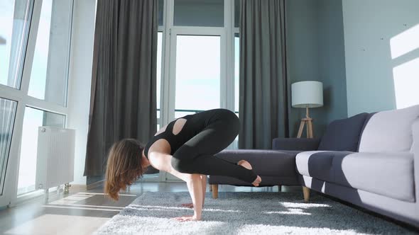 Young Caucasian Woman in Black Jumpsuit Doing Handstand Bakasana at Home to Develop Power