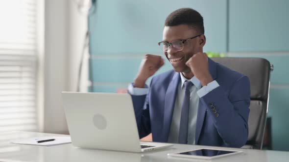 Young African Businessman Celebrating Success While Using Laptop in Office