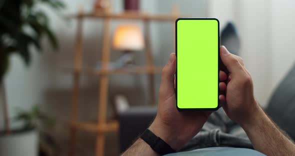 Man Touching Smartphone Green Screen While Lying on Sofa, Guy Using Phone with Mocked Up Display