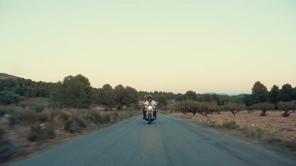 Couple Riding Cruiser Motorcycle At Countryside Road During Sunset. - front view, pullback