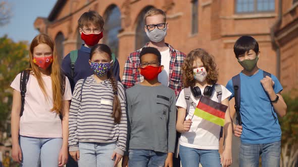 Portrait of Diverse Kids and Teacher in Medical Mask Standing Outdoors with German Flag