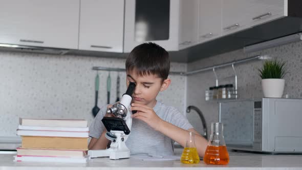A Boy Learns Biology Using a Microscope and Makes Notes in a Notebook. Homework.