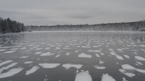 Aerial flight over frozen lake with fresh snowfall surrounded by forestry