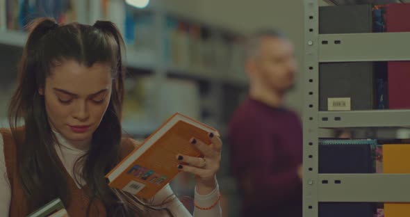 Beautiful Student Girl Takes Books From the Shelf and Moves Away From the Bookcase