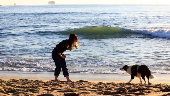 Woman playing with her dog on the beach at sunset.