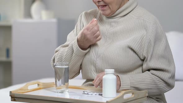 Elderly Female Patient Taking Pill and Drinking Water in Hospital Room, Medicare