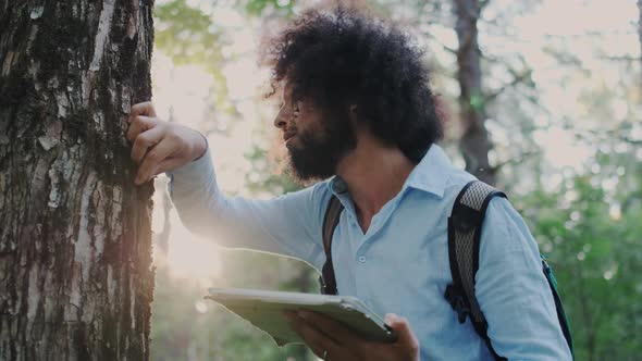 Male Curly Environmentalist Inspecting and Analyze Cover of Tree and Wood in Forest