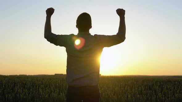 Silhouette of a Farmer Standing in a Field with Arms Raised