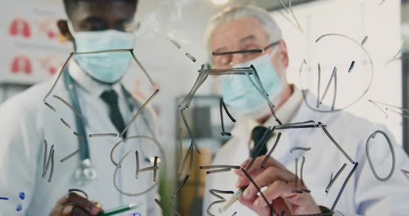 Mixed Race Doctors in Sterile Medical Masks which Discussing Chemical Formula Drawn on this Wall