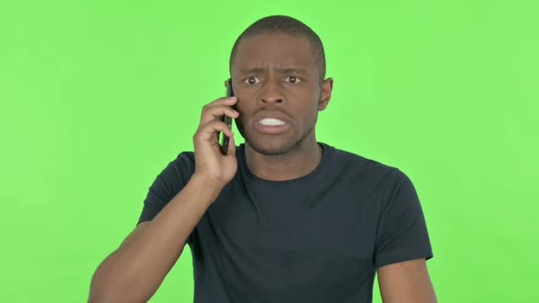 Angry Young African Man Talking on Phone on Green Background