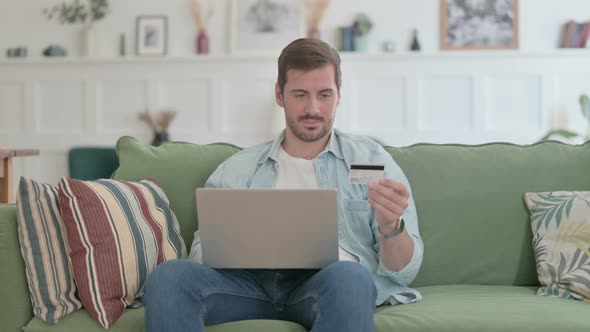 Young Man Making Online Payment on Laptop on Sofa