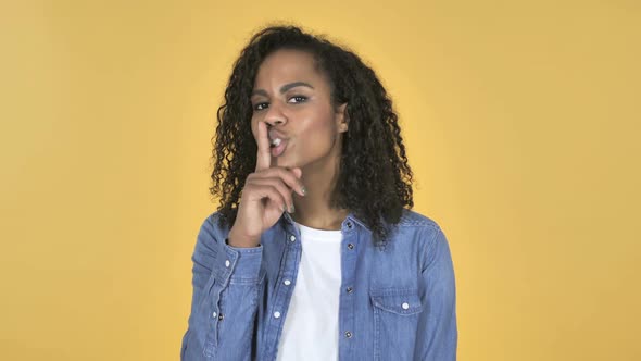 African Girl Gesturing Silence Finger on Lips Yellow Background