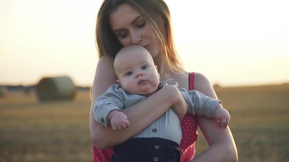 Portrait of Happy Mother Caresses and Embraces Baby Son with Harmony in Field