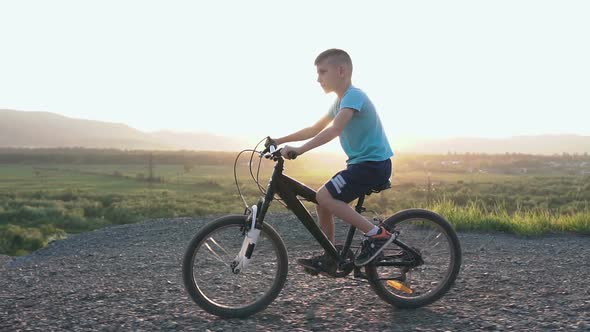 Beautiful Little Boy Who Rides a Black Bike in a Mountainous Place in the Summer alt