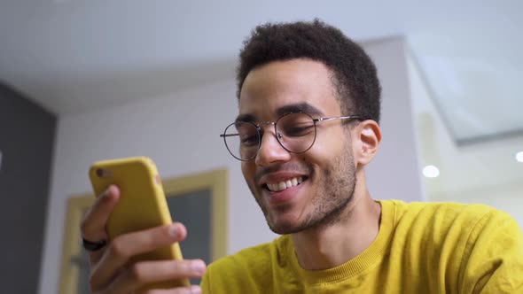 A Young Happy African Man Smiles and Texts on His Smartphone