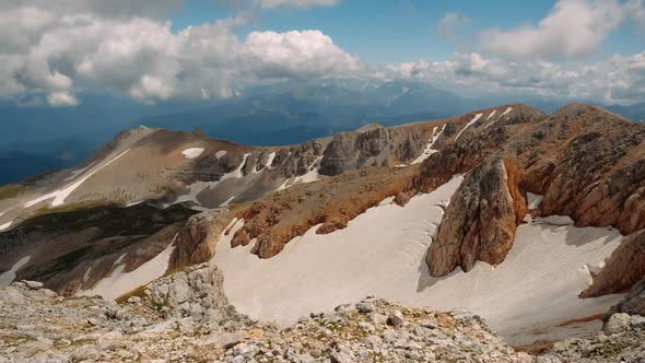 Flight Over Unusual Brown Gray Mountain Covered with Snow Against Background of Silhouettes of Large