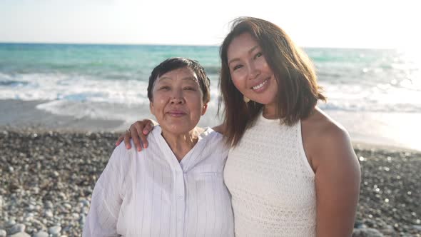 Portrait of Gorgeous Adult Asian Woman and Senior Happy Retiree Standing at Sunset on Mediterranean