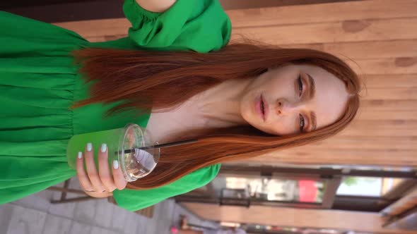 Front View of Happy Female Blogger Holding Camera in Hand Recording Video Drinking Cold Cocktail