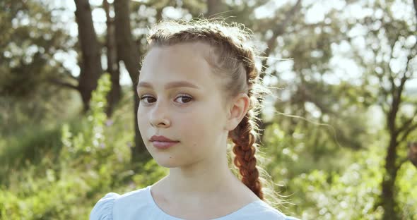 Attractive European Chestnut Teen Girl with Natural Makeup Looks Into the Camera in Nature on a
