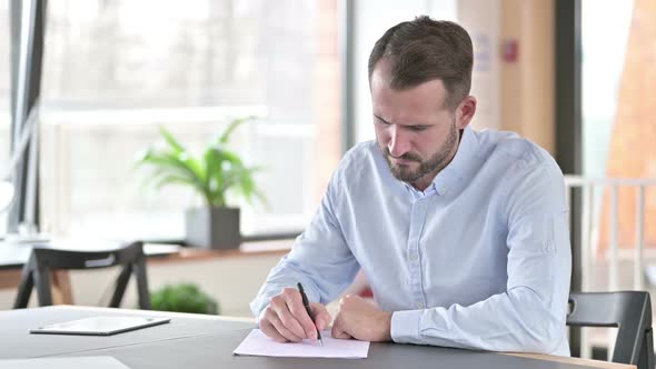 Disappointed Young Man Trying to Do Paperwork in Office