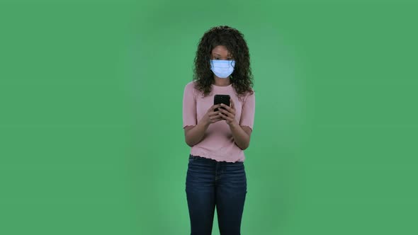 Portrait of Beautiful African American Young Woman in Medical Mask Is Texting on Her Phone. Burning