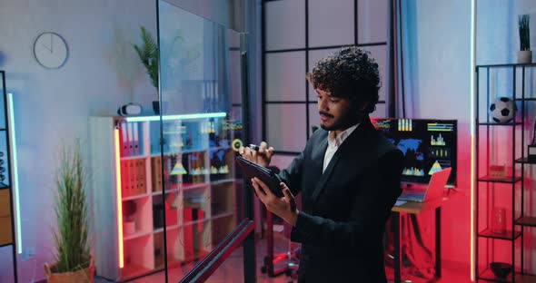 Muslim Office Worker in Suit Writing Needed Notes on Glass wall from Tablet pc When Working Overtime