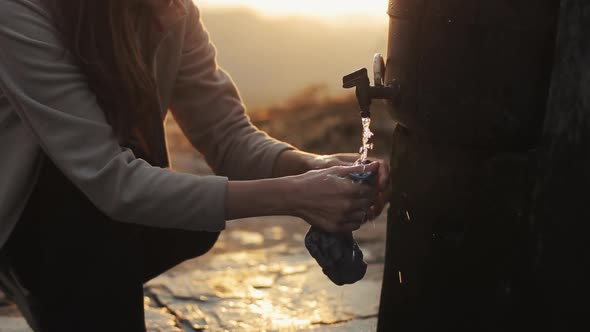 A Close Up on a Caucasian Young Woman Washing Clothes Under a Public Faucet. Village, Morning.