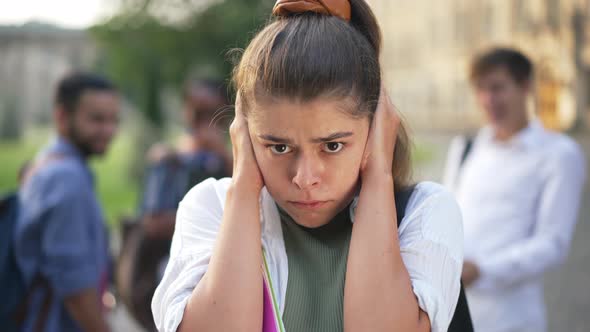 Scared Stressed Young Beautiful Woman with Hands Covering Ears Looking at Camera As Blurred