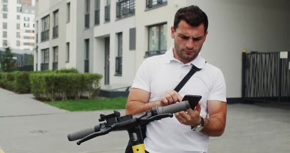 Trendy Man with Escooter Using Smartphone for Mobile Call in Summer City