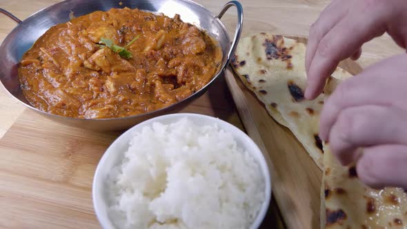 Slider Shot of Tearing off a Piece of Butter Naan and Dipping it in a Homemade Indian Curry in a Bal