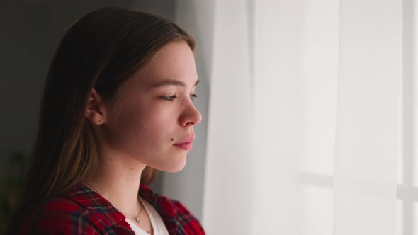 Depressed Woman Stands Looking Out of Window in Apartment