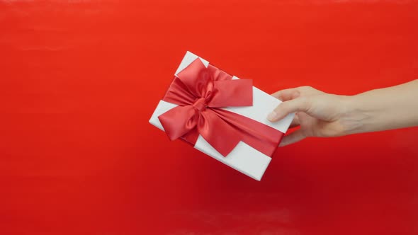 Woman hand gives present box to man hand on red background. Gift for St. Valentine's Day or Birthday