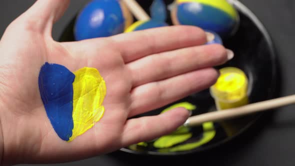 Painted Female Hand in YellowBlue Color on the Background of Easter Eggs
